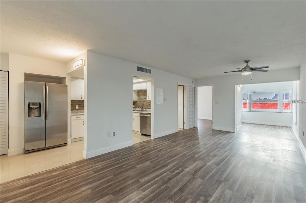 A living area with wood-look flooring leads to a kitchen and a sunroom with windows — 6100 12TH STREET S UNIT 315, ST PETERSBURG, FL