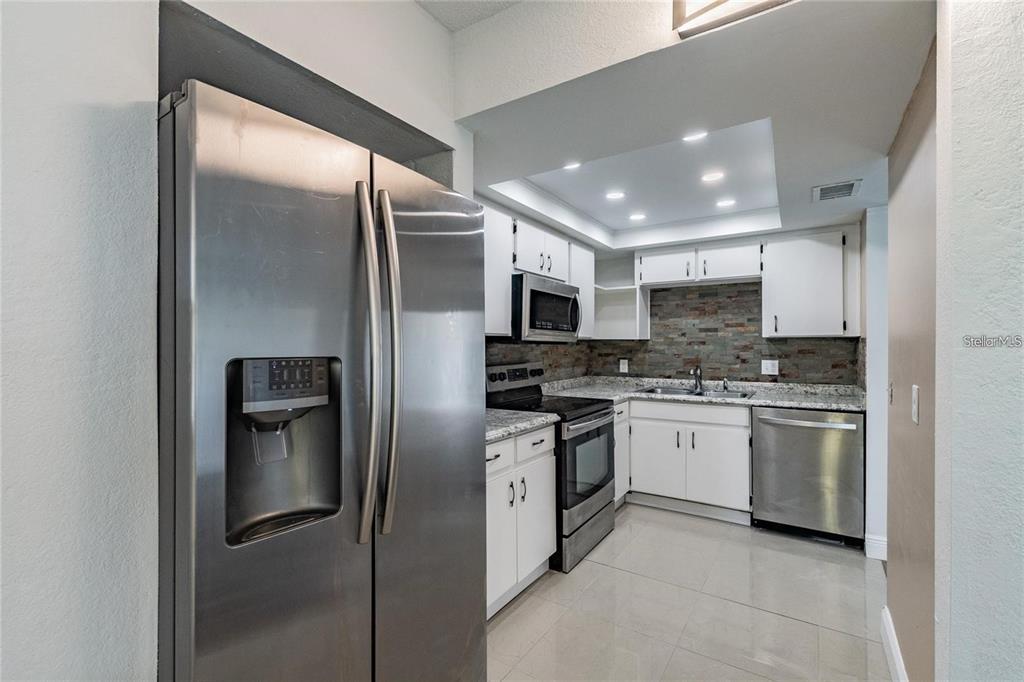 A kitchen features stainless steel appliances, white cabinets, granite countertops, and a stone tile backsplash — 6100 12TH STREET S UNIT 315, ST PETERSBURG, FL