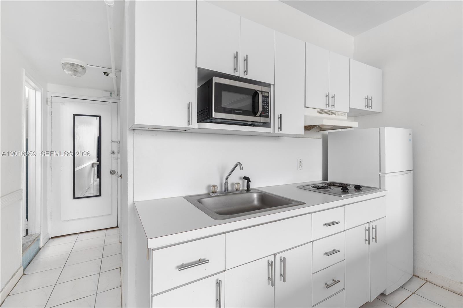 A small kitchen features white cabinets, a stainless steel sink, and a built-in microwave — 255 W 24th St # 432, Miami Beach FL 33140, MIAMI BEACH, FL