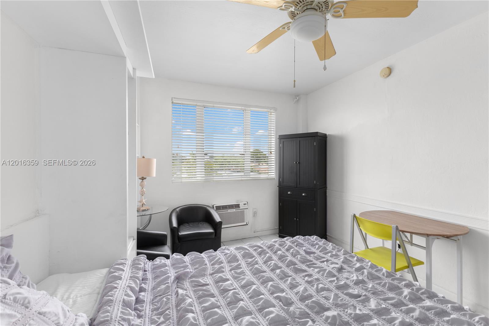 A bedroom features a bed, a black cabinet, a small table with chairs, and a window — 255 W 24th St # 432, Miami Beach FL 33140, MIAMI BEACH, FL