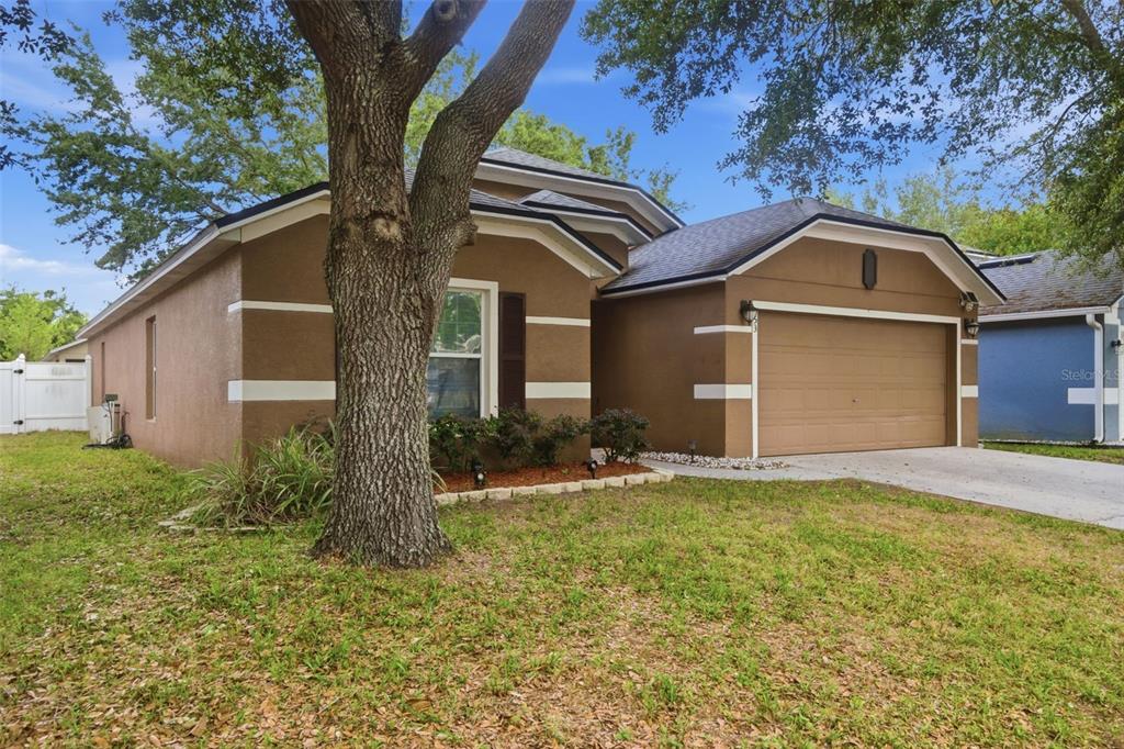 A brown single-story house with a two-car garage and a large tree in the yard — 553 MAIDENHAIR COURT, ORANGE CITY, FL