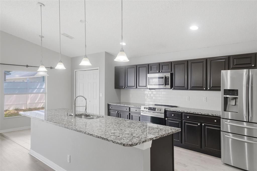 A kitchen features dark cabinets, granite countertops, stainless steel appliances, and a large island — 553 MAIDENHAIR COURT, ORANGE CITY, FL