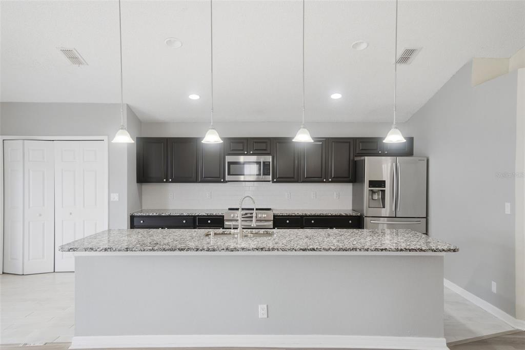 A kitchen features dark cabinets, stainless steel appliances, a granite island, and four pendant lights — 553 MAIDENHAIR COURT, ORANGE CITY, FL