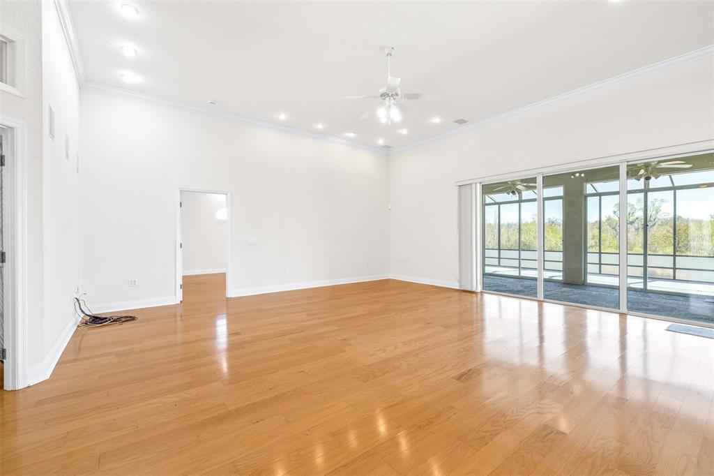 An empty living room with hardwood floors, a ceiling fan, and large sliding glass doors — 6779 HUNTINGTON HILLS BOULEVARD, LAKELAND, FL