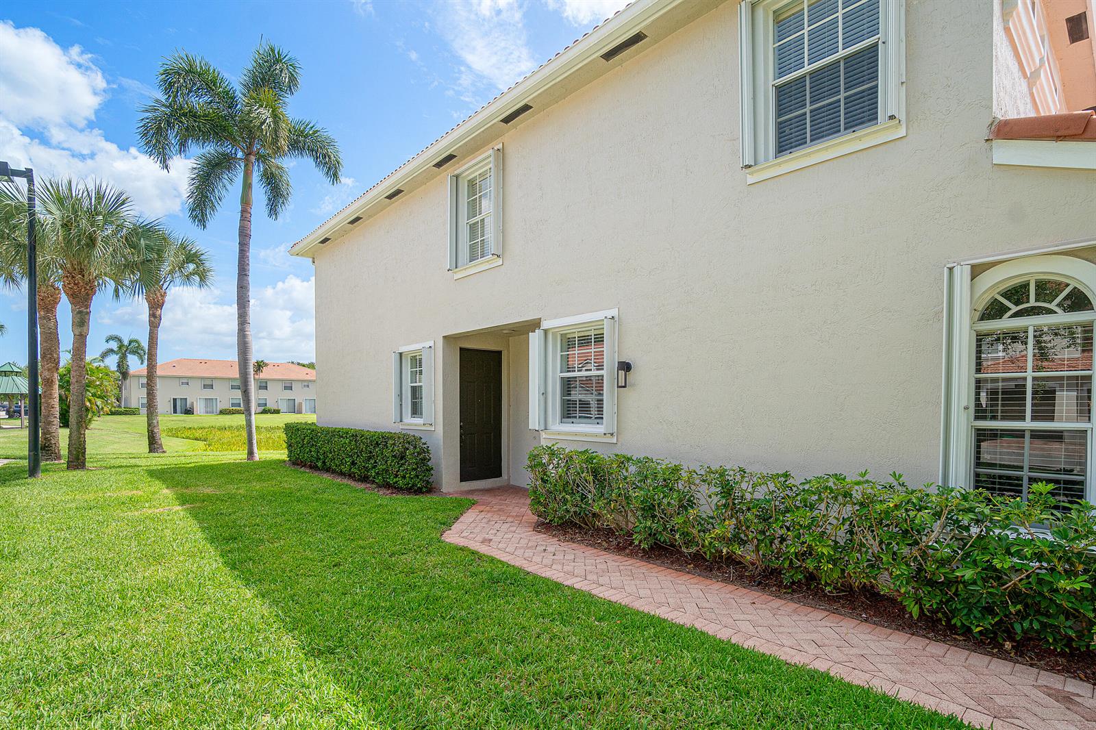 A beige two-story building exterior features a brick walkway leading to a dark front door — 16122 Poppy Seed Circle Unit 1401, Delray Beach FL 33484, DELRAY BEACH, FL