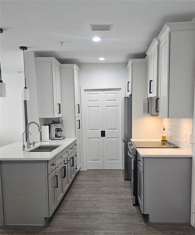 A modern kitchen features white cabinets, gray lower cabinets, quartz countertops, and stainless steel appliances — 5550 E MICHIGAN STREET UNIT 2228, ORLANDO, FL