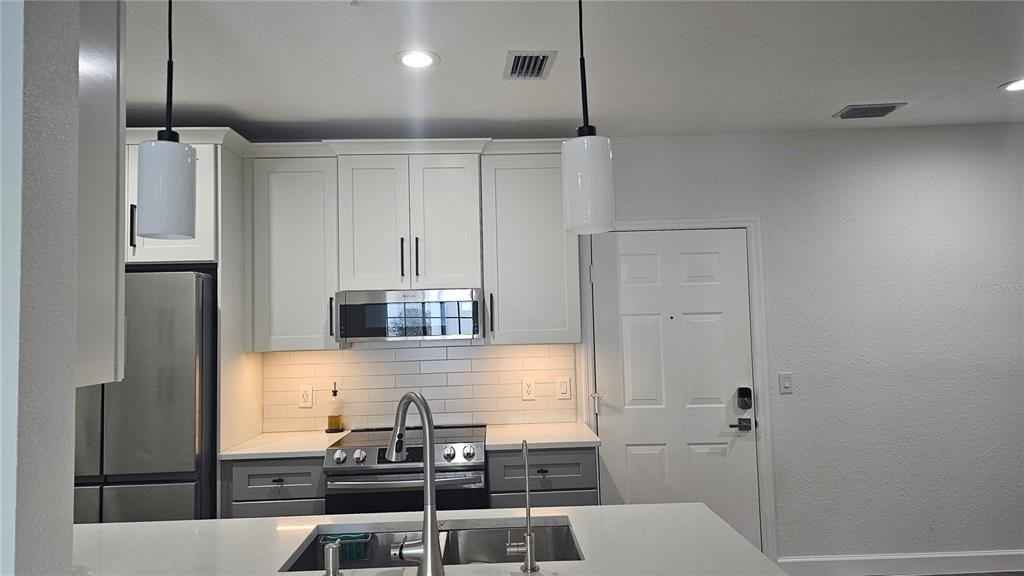 A modern kitchen features white upper cabinets, gray lower cabinets, stainless steel appliances, and an island — 5550 E MICHIGAN STREET UNIT 2228, ORLANDO, FL