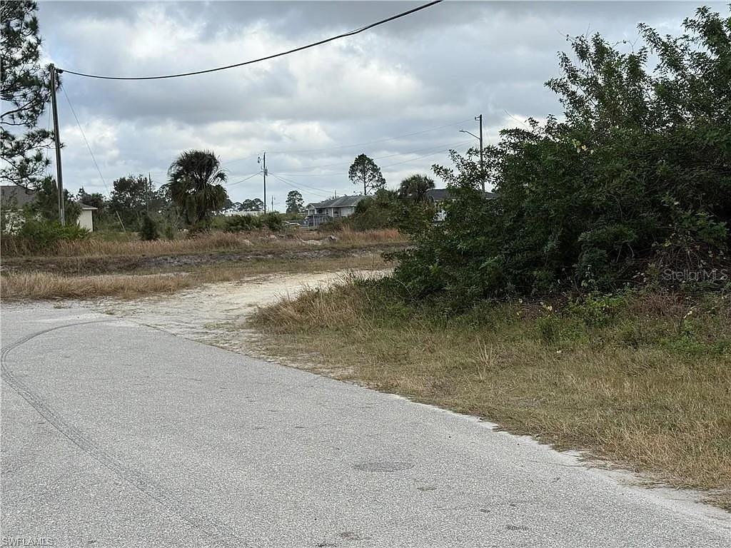 A paved road leads to an undeveloped, grassy lot with scattered trees and utility poles — 3101 67TH STREET W, LEHIGH ACRES, FL
