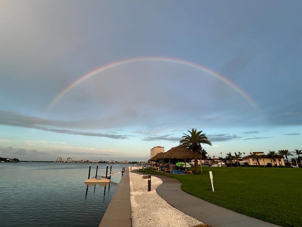 A rainbow arches over a waterfront park with a paved path, palm trees, and docks — 4900 BRITTANY DRIVE S UNIT 1003, ST PETERSBURG, FL