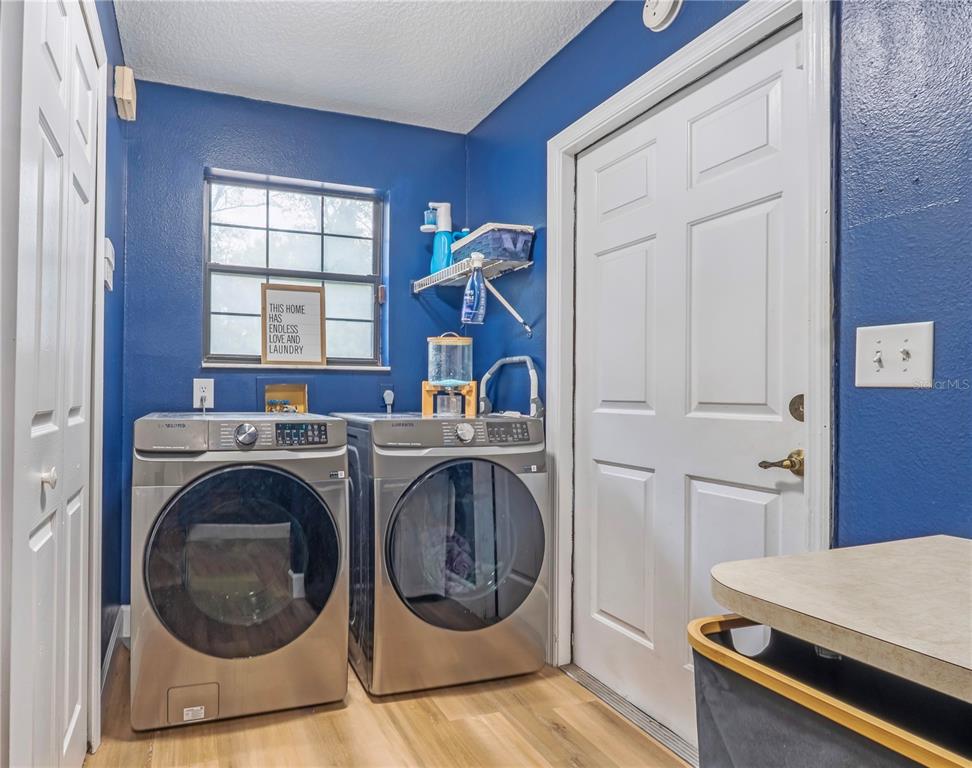 A laundry room features blue walls, wood-look flooring, and a pair of stainless steel appliances — 425 BLACK IRONWOOD DRIVE, DELAND, FL