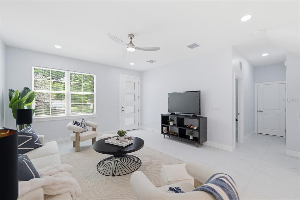 A bright living room features white walls, tile flooring, a ceiling fan, and modern furniture — 8119 N DAKOTA AVENUE, TAMPA, FL