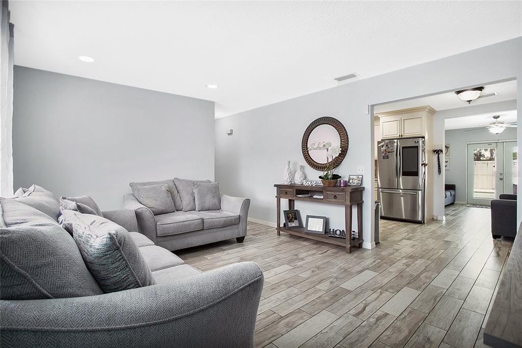 A living room with gray sofas, wood-look tile flooring, and a view into the kitchen — 614 SIDNEY CIRCLE, WINTER HAVEN, FL
