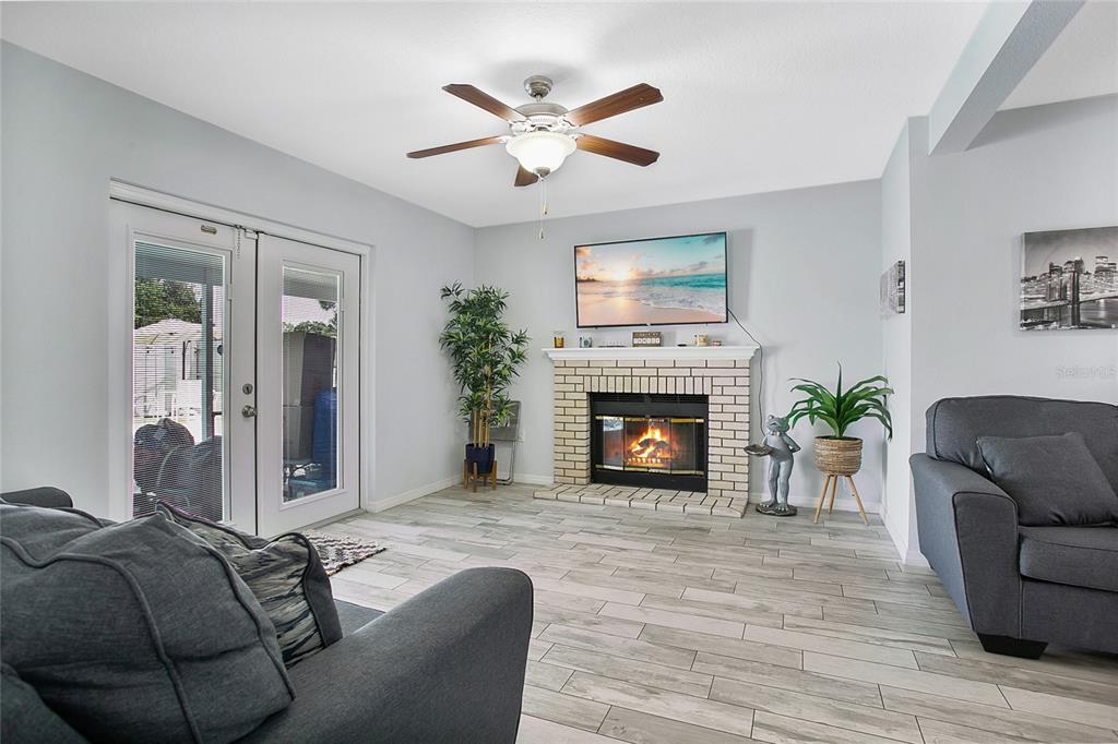 A living room features a brick fireplace, a ceiling fan, and gray tile flooring — 614 SIDNEY CIRCLE, WINTER HAVEN, FL