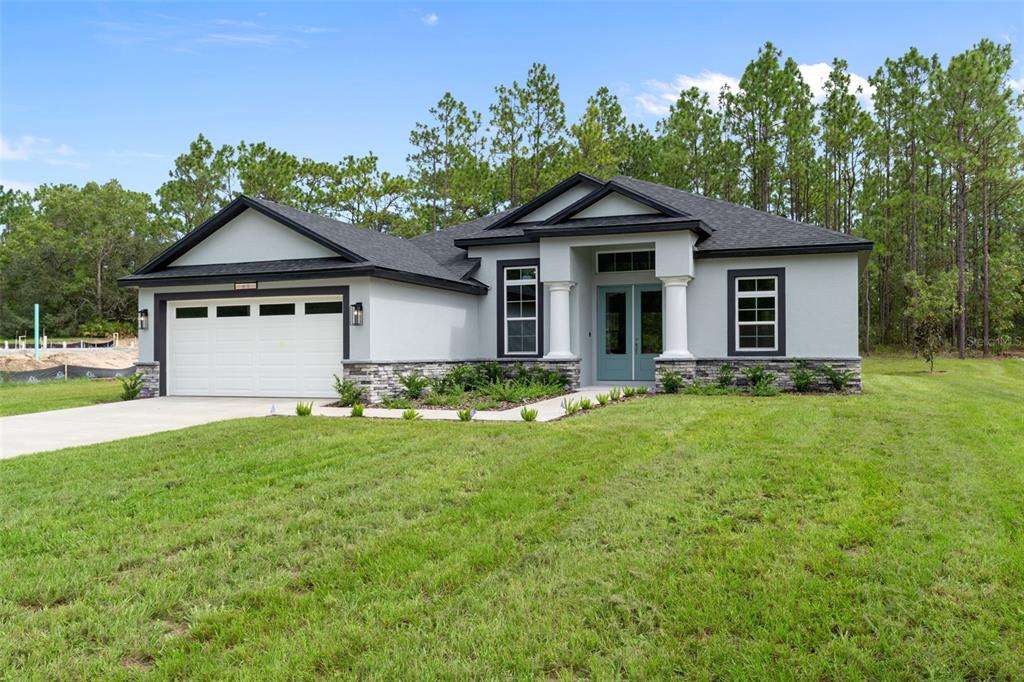 A single-story house with a white garage, gray stucco exterior, stone accents, and a front porch — 60 CORKWOOD BOULEVARD, HOMOSASSA, FL