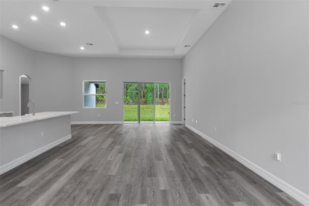An open-concept living area features gray wood-look flooring, a tray ceiling, and sliding glass doors — 60 CORKWOOD BOULEVARD, HOMOSASSA, FL