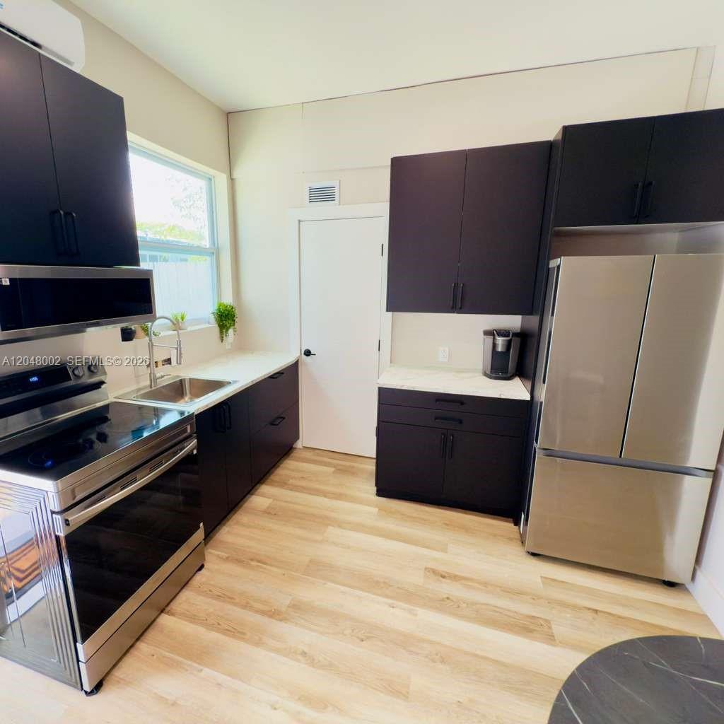 A modern kitchen features dark cabinetry, stainless steel appliances, and light wood-look flooring — 220 NW 126th St # B, North Miami FL 33168, NORTH MIAMI, FL