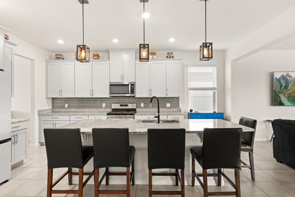 A kitchen features white cabinets, granite countertops, a central island with seating, and pendant lighting — 660 BIG PINE AVENUE, MINNEOLA, FL