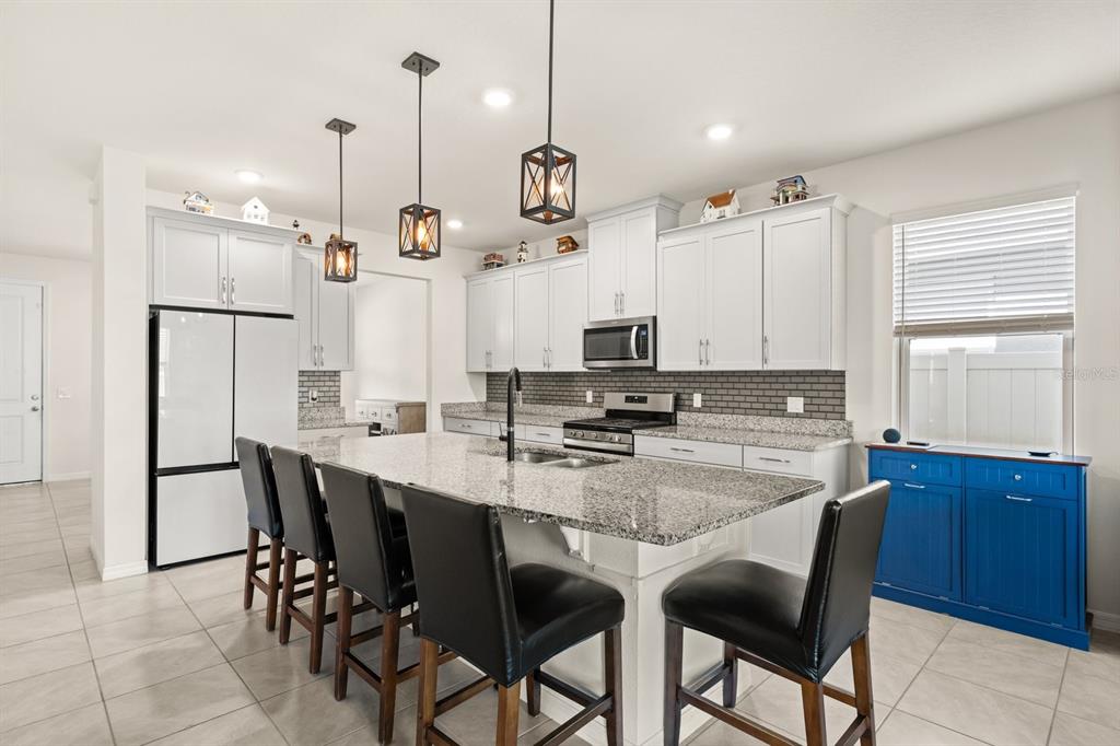 A kitchen features white cabinetry, granite countertops, a central island with seating, and blue cabinets — 660 BIG PINE AVENUE, MINNEOLA, FL
