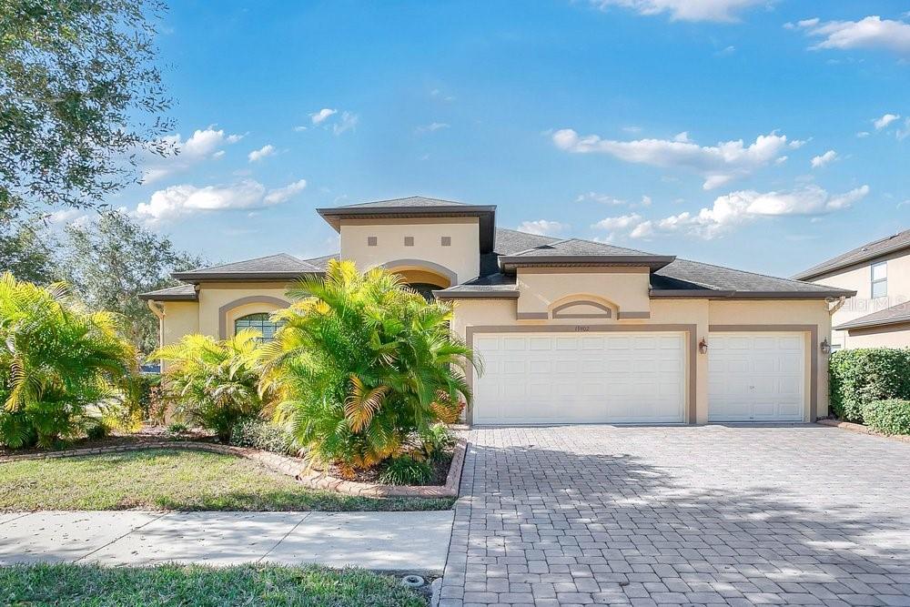 A single-story house with a beige stucco exterior, a three-car garage, and a paved driveway — 19402 SWEET GRASS WAY, LUTZ, FL