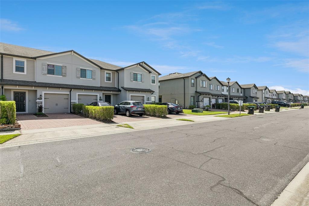 A row of two-story townhomes with attached garages and paved driveways under a blue sky — 1283 FLOWING TIDE DRIVE, ORLANDO, FL