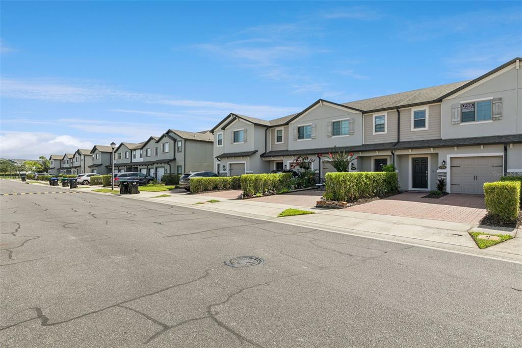 A row of multi-story townhouses with attached garages and paved driveways under a blue sky — 1283 FLOWING TIDE DRIVE, ORLANDO, FL