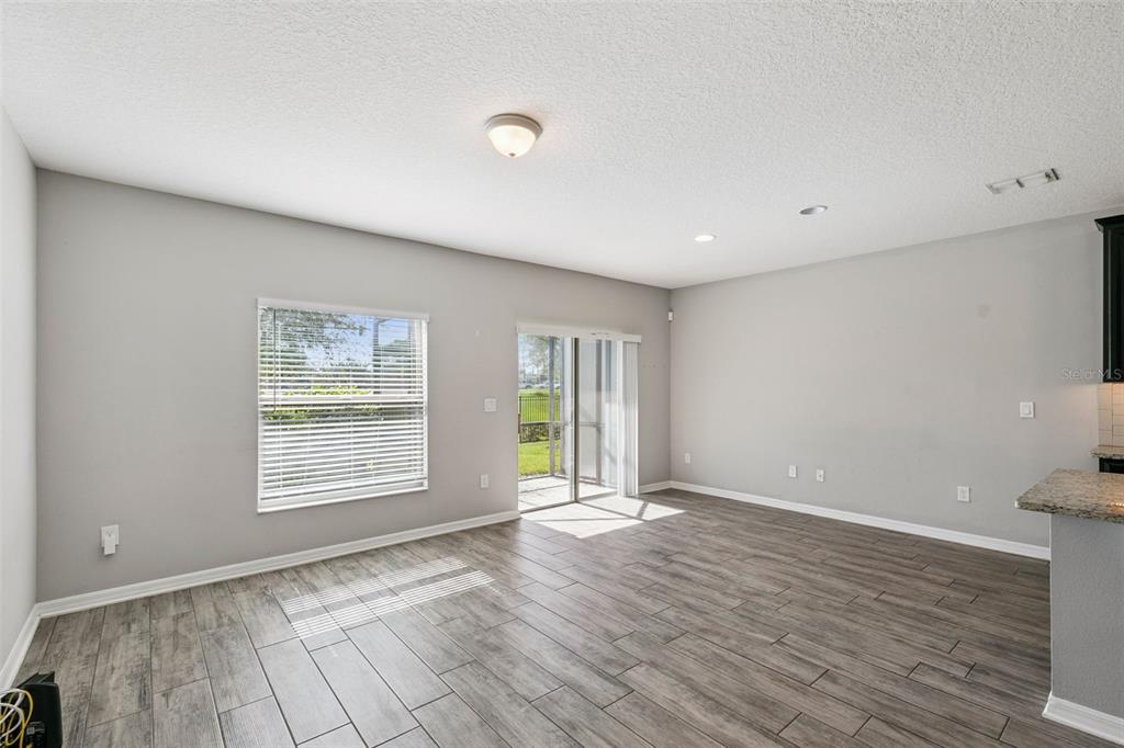 An empty living room features gray walls, wood-look tile flooring, a sliding glass door, and windows — 1283 FLOWING TIDE DRIVE, ORLANDO, FL