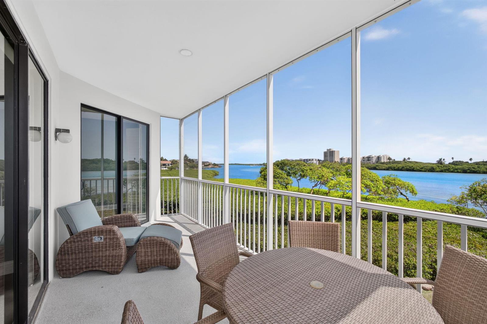 A screened-in balcony features wicker furniture overlooking a waterway and coastal landscape — 200 Waterway Road # 206, Tequesta FL 33469, TEQUESTA, FL