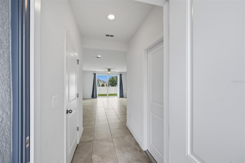 A hallway with tile flooring leads to an open living area with sliding glass doors — 14087 LILAC SKY TERRACE, LAKEWOOD RANCH, FL