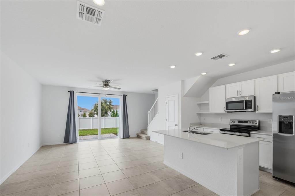 An open-concept kitchen and living area with white cabinets, tile flooring, and sliding glass doors — 14087 LILAC SKY TERRACE, LAKEWOOD RANCH, FL