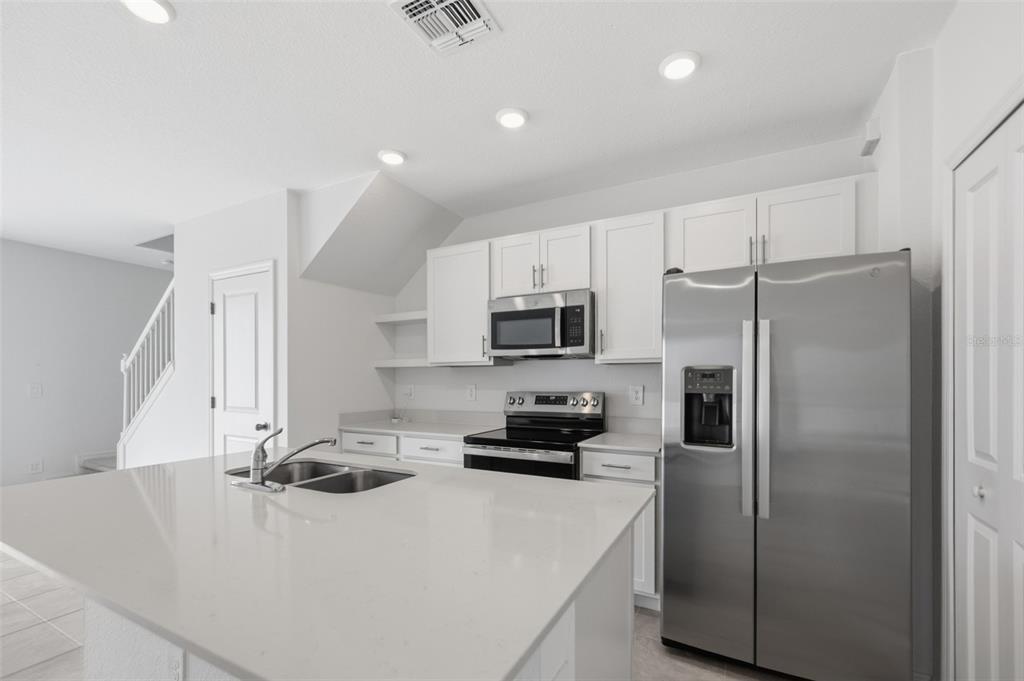 A modern kitchen features white cabinets, stainless steel appliances, and a large quartz-topped island — 14087 LILAC SKY TERRACE, LAKEWOOD RANCH, FL
