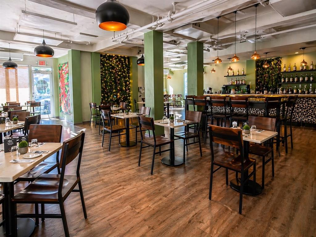 A restaurant interior features wooden tables, dark chairs, green pillars, and hanging pendant lights — 619 CALLE CERRA, SAN JUAN, PR