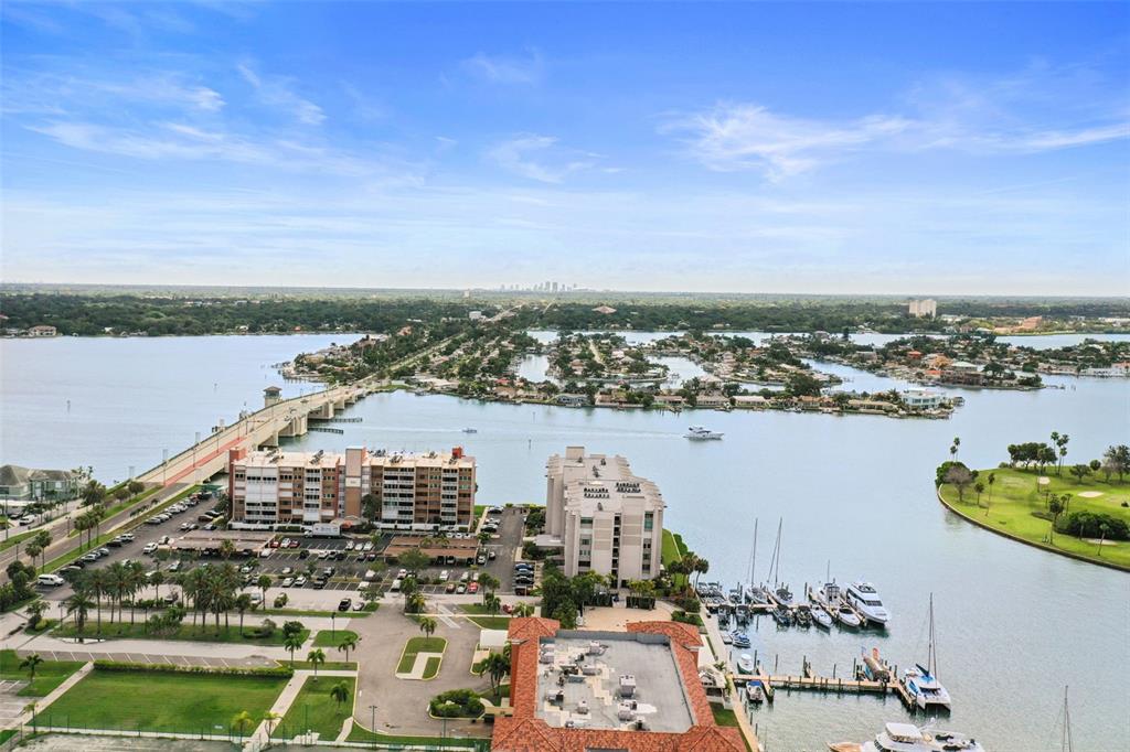 An aerial view shows a bridge, waterfront apartment buildings, a marina, and a golf course — 500 TREASURE ISLAND CAUSEWAY UNIT 610, TREASURE ISLAND, FL