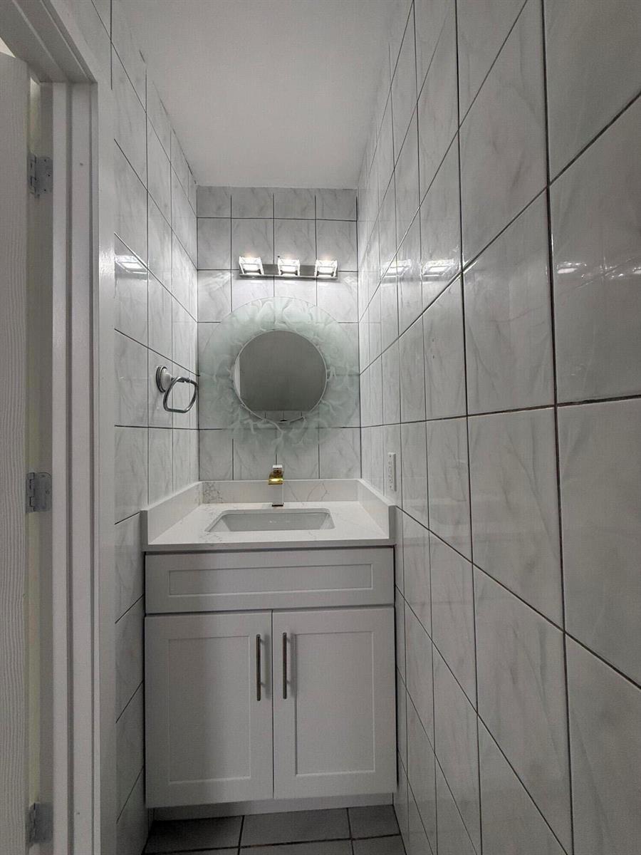 A small bathroom features white tiled walls, a vanity with a white countertop, and a mirror — 4415 SW 72nd Terrace, Davie FL 33314, DAVIE, FL