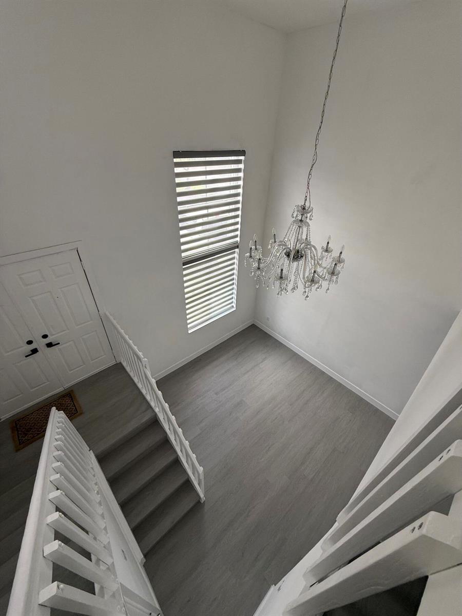 A high-ceilinged entryway features gray wood-look flooring, a crystal chandelier, and a white staircase — 4415 SW 72nd Terrace, Davie FL 33314, DAVIE, FL