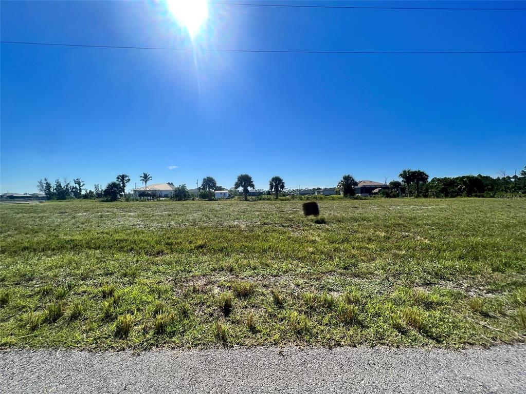 A flat, grassy vacant lot under a clear blue sky with distant houses and trees — 4008 NW 42ND PLACE, CAPE CORAL, FL