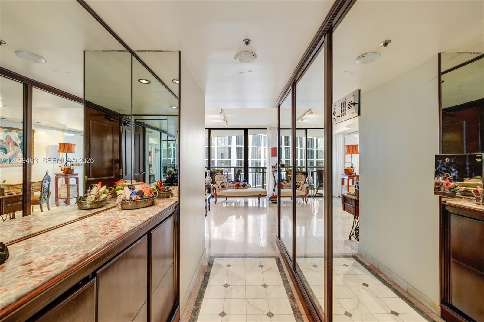 A hallway with mirrored walls and marble flooring leads toward a bright living area — 2843 S Bayshore Dr # 11F, Miami FL 33133, MIAMI, FL