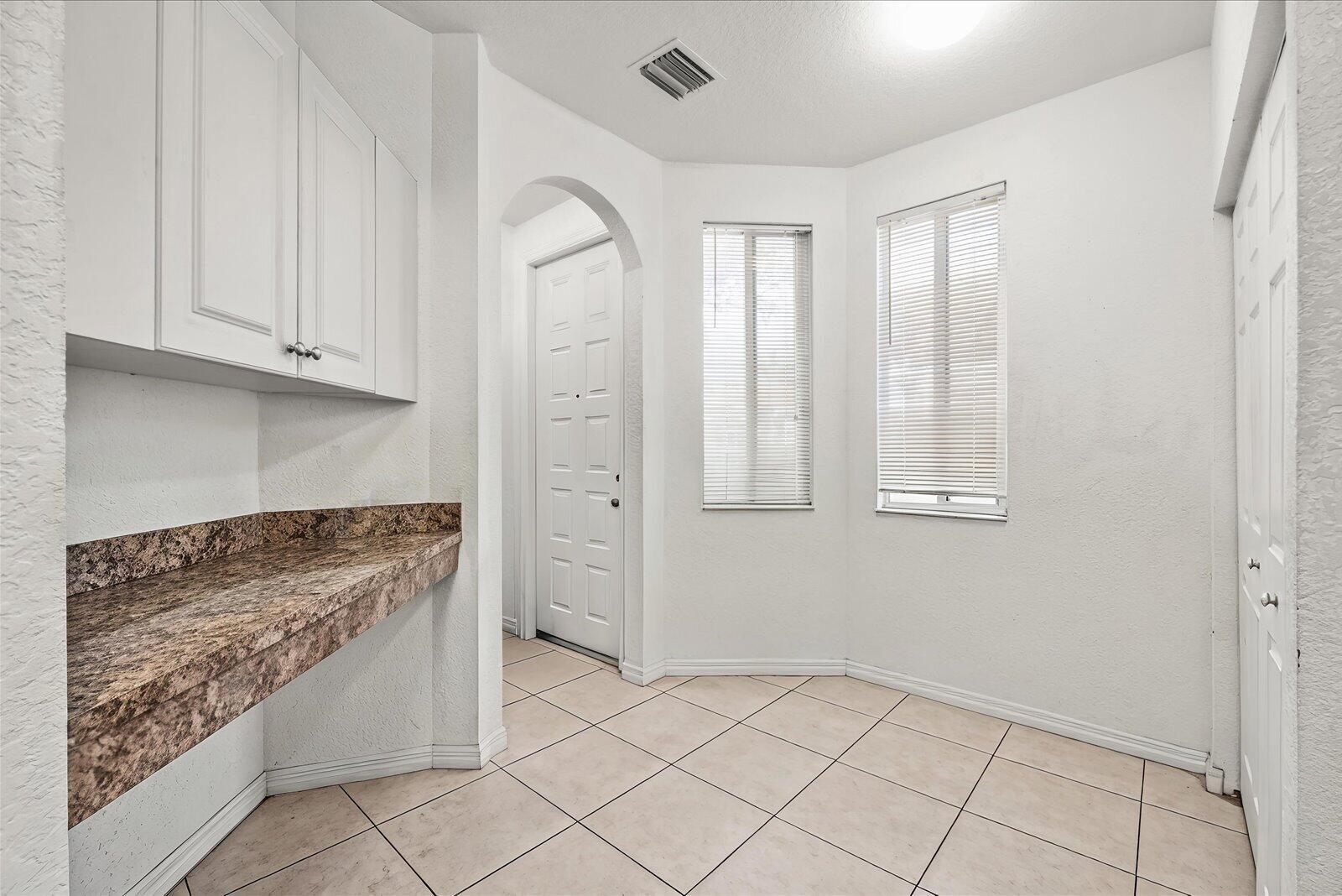 A laundry room with white cabinets, a brown granite countertop, and light-colored tile flooring — 3529 Sonoma Drive, Riviera Beach FL 33404, RIVIERA BEACH, FL