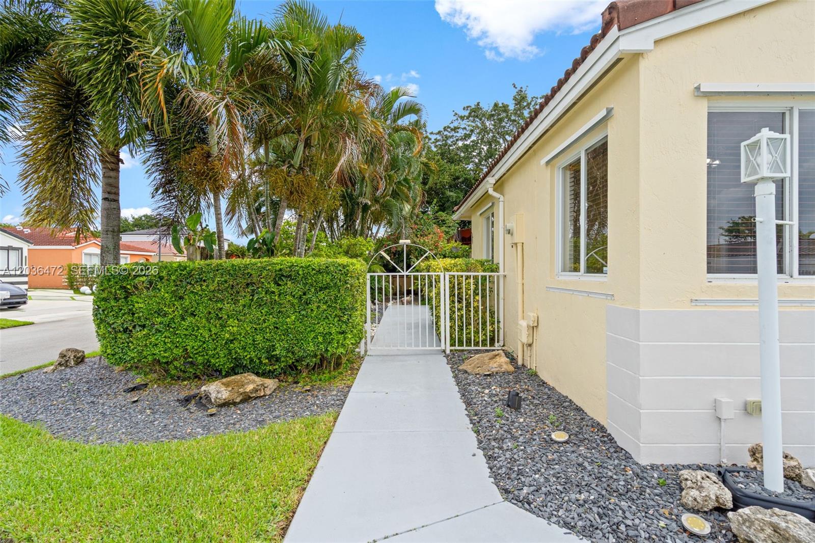 A concrete walkway leads to a white metal gate beside a light-colored house exterior — 14365 SW 175th Ter, Miami FL 33177, MIAMI, FL