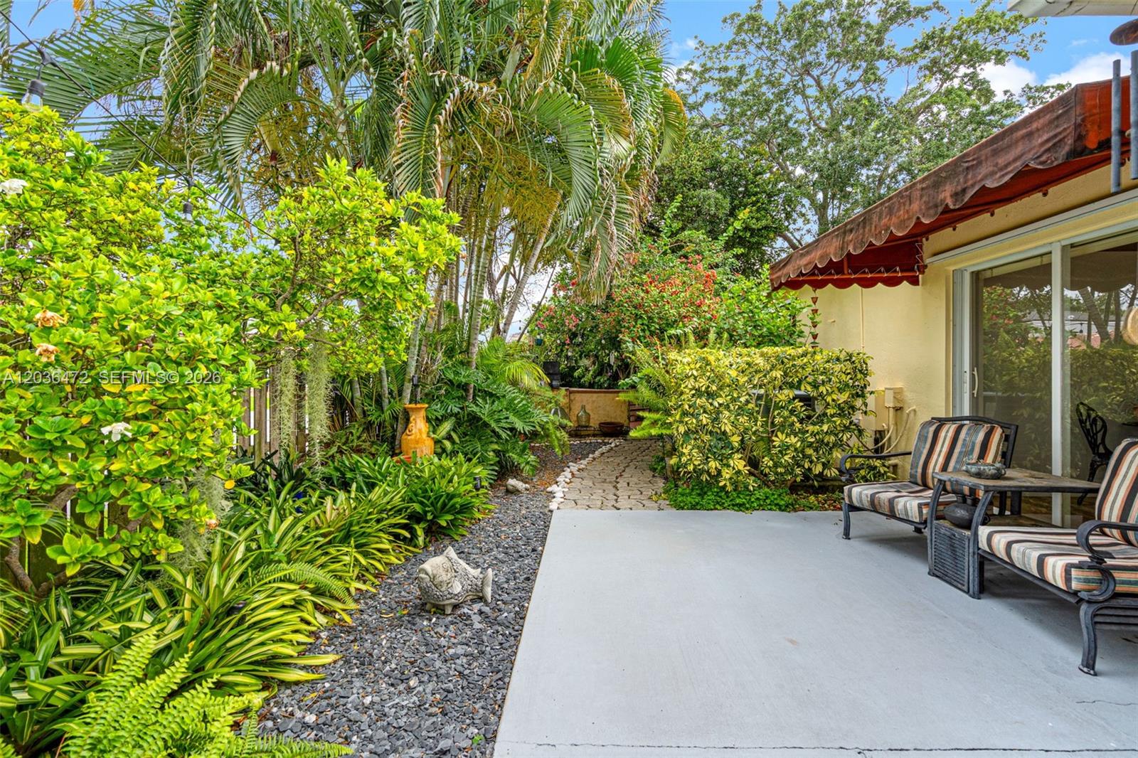 A patio with striped chairs sits next to a garden with a stone path — 14365 SW 175th Ter, Miami FL 33177, MIAMI, FL