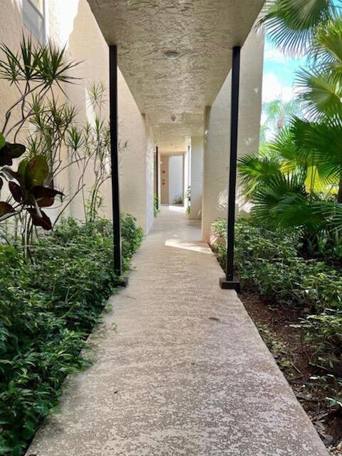 A concrete walkway leads through a covered outdoor corridor flanked by lush green landscaping — 7472 La Paz Boulevard # 103, Boca Raton FL 33433, BOCA RATON, FL