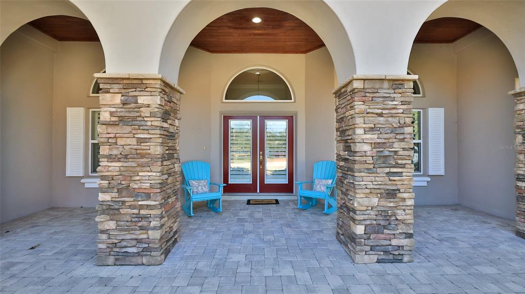 A covered front porch features stone columns, arched openings, a wood ceiling, and two blue chairs — 2904 PALMA LANE, NEW SMYRNA BEACH, FL