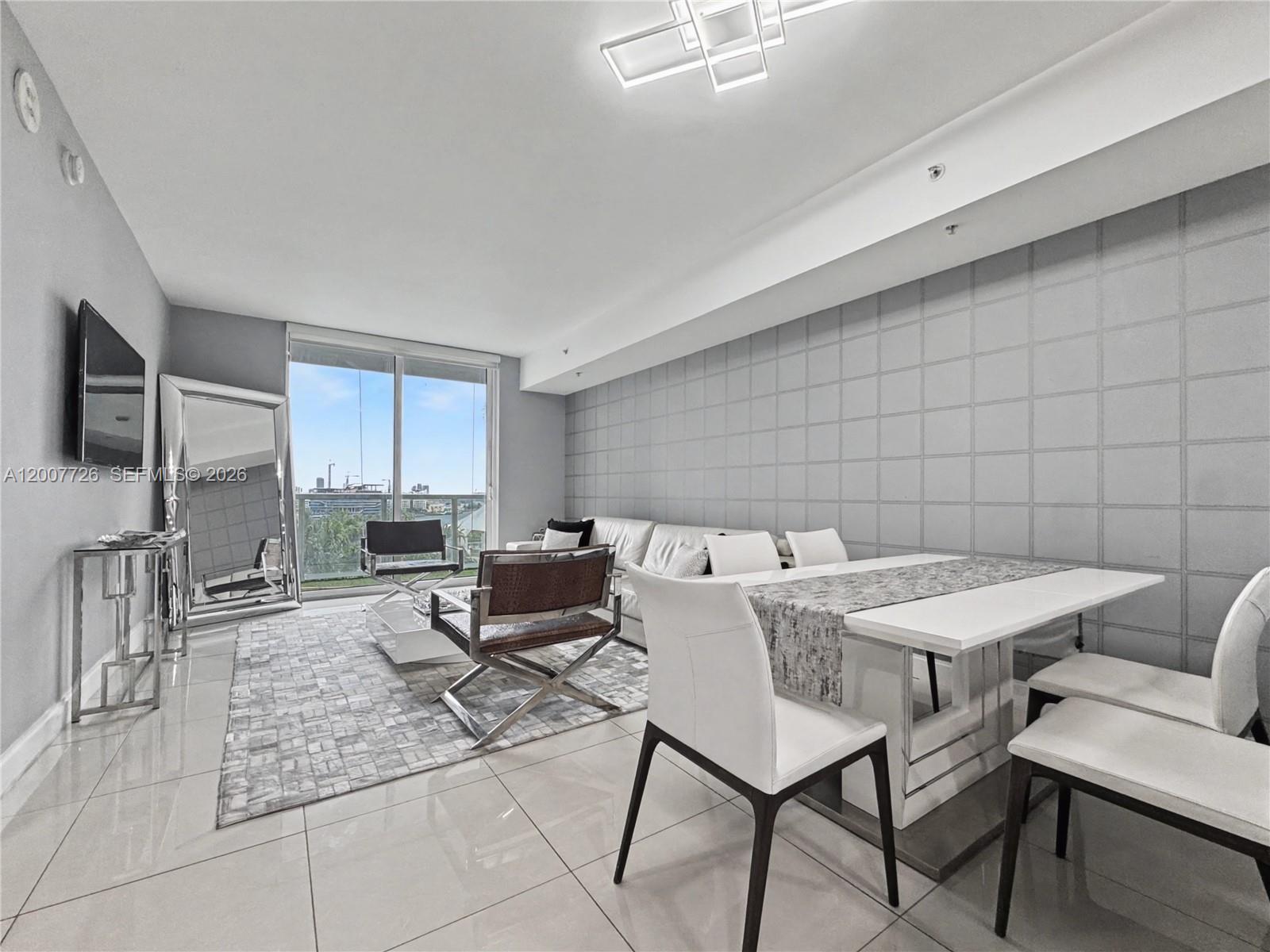 A modern living and dining area features white tile floors, a grid-patterned wall, and balcony — 253 NE 2nd St # 1003, Miami FL 33132, MIAMI, FL