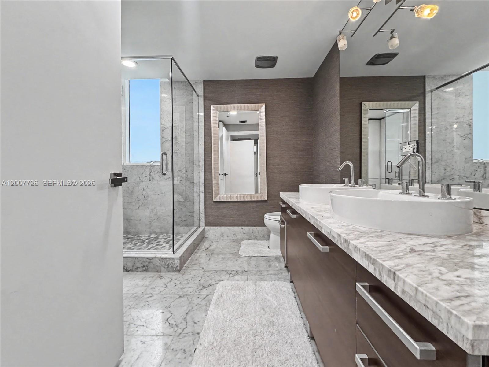 A modern bathroom features a double vanity, marble countertops, a glass shower, and textured walls — 253 NE 2nd St # 1003, Miami FL 33132, MIAMI, FL