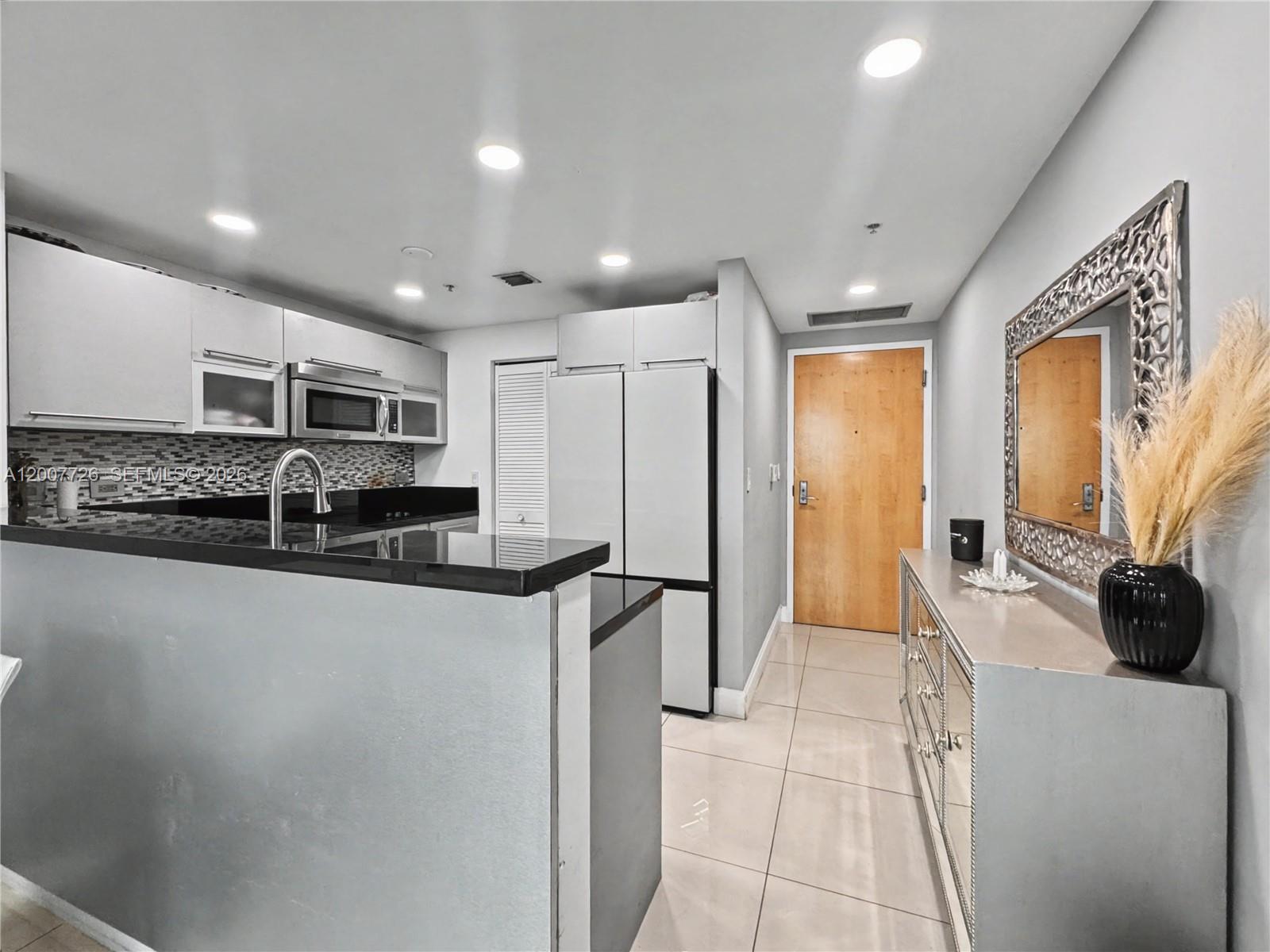 A kitchen features a black countertop, stainless steel appliances, and a mirrored console table nearby — 253 NE 2nd St # 1003, Miami FL 33132, MIAMI, FL