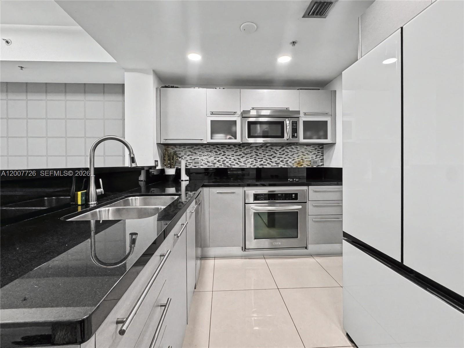 A modern kitchen features stainless steel appliances, black countertops, and light-colored cabinetry — 253 NE 2nd St # 1003, Miami FL 33132, MIAMI, FL