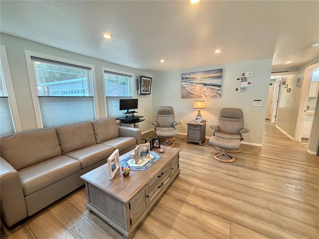 A living room features a grey sofa, two recliners, a wooden coffee table, and light-colored flooring — 121 TAMARISK WAY, LEESBURG, FL