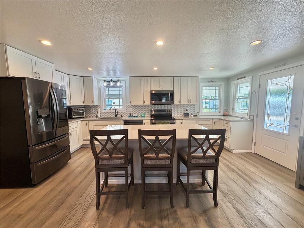 A modern kitchen features white cabinetry, a central island with three stools, and wood-look flooring — 121 TAMARISK WAY, LEESBURG, FL