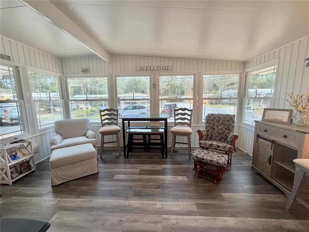 A sunroom with wood-look flooring, large windows, a small dining set, and two armchairs — 121 TAMARISK WAY, LEESBURG, FL