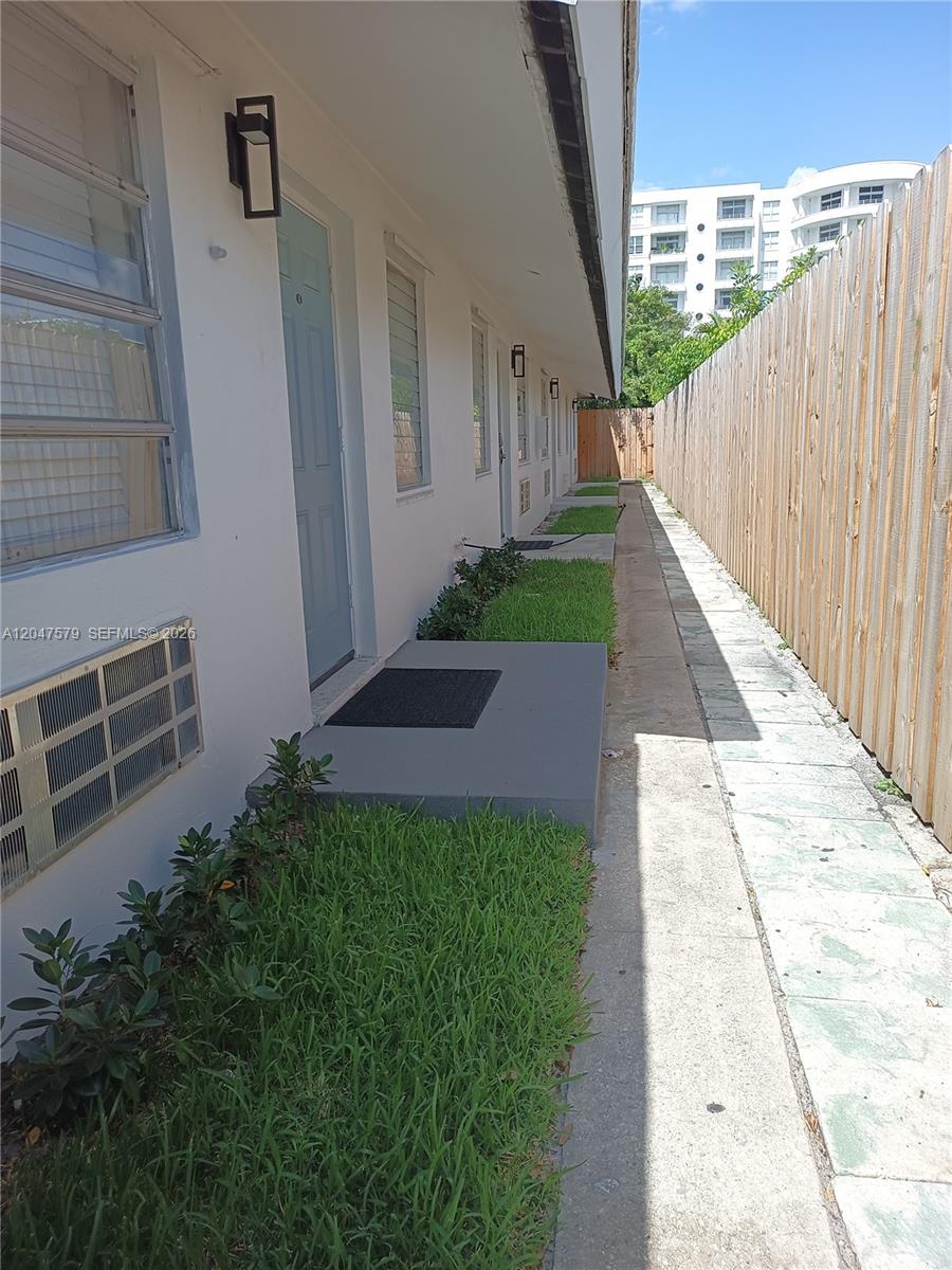 A narrow concrete walkway runs between a white building with several doors and a wooden fence — FORT LAUDERDALE, FL