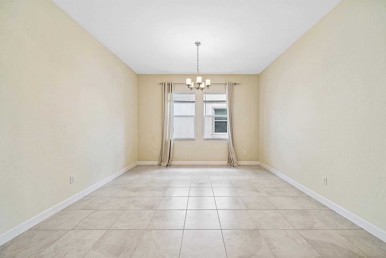 An empty dining room features light-colored tile flooring, beige walls, and a central chandelier — 1031 Ember Ridge Run, Loxahatchee FL 33470, LOXAHATCHEE, FL